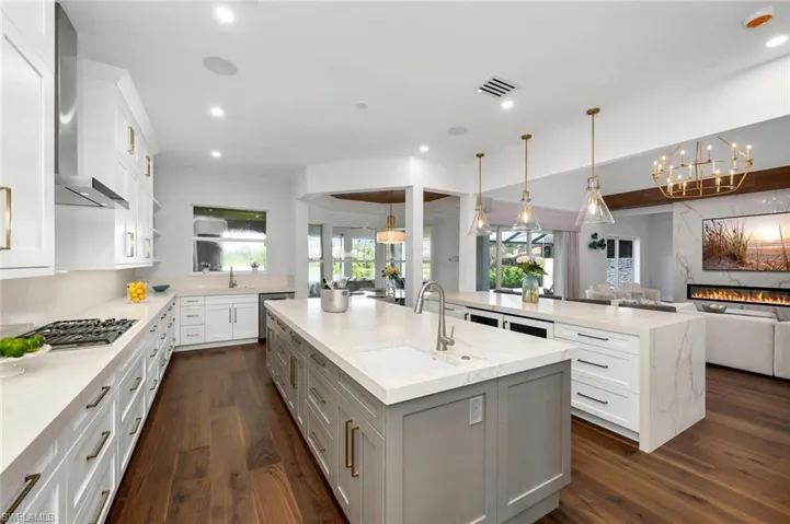 Kitchen featuring a large island with sink, decorative light fixtures, and light stone counters