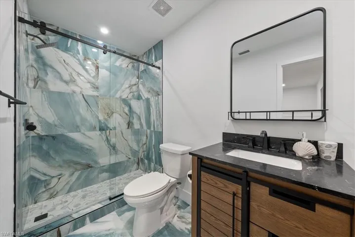 Full bathroom with vanity, a marble finish shower, and recessed lighting
