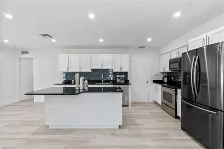 Kitchen with stainless steel appliances, backsplash, a kitchen island, white cabinetry, and light wood-style flooring