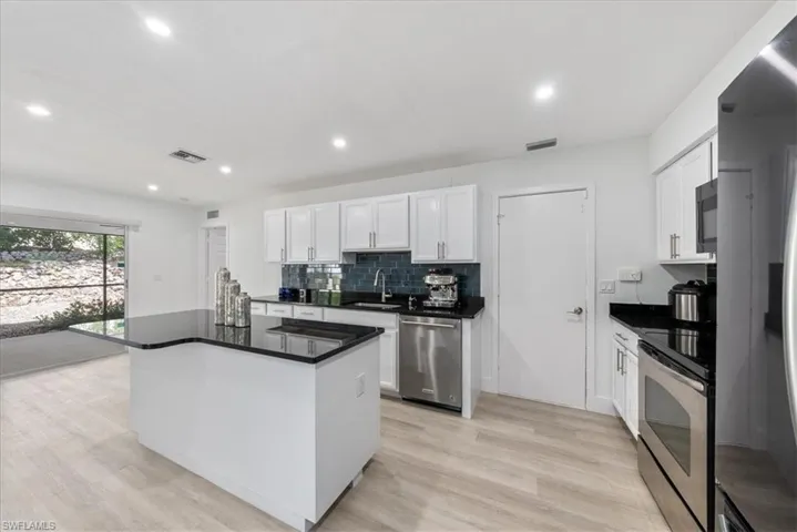 Kitchen with backsplash, white cabinetry, stainless steel appliances, a kitchen island, and recessed lighting