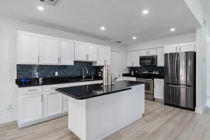Kitchen featuring appliances with stainless steel finishes, white cabinets, tasteful backsplash, light wood-type flooring, and recessed lighting