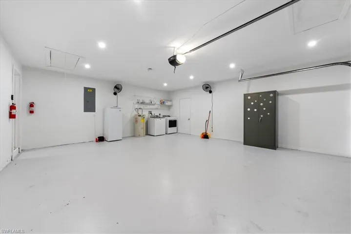 Garage with washing machine and dryer, white fridge, electric panel, recessed lighting, and electric water heater