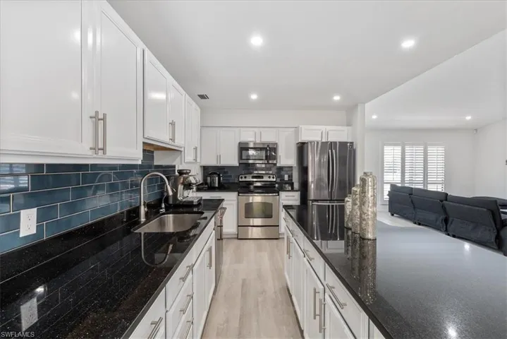 Kitchen featuring backsplash, dark stone countertops, appliances with stainless steel finishes, white cabinetry, and light wood-style flooring