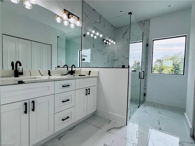 Full bath with marble finish floor, a sink, a marble finish shower, and double vanity