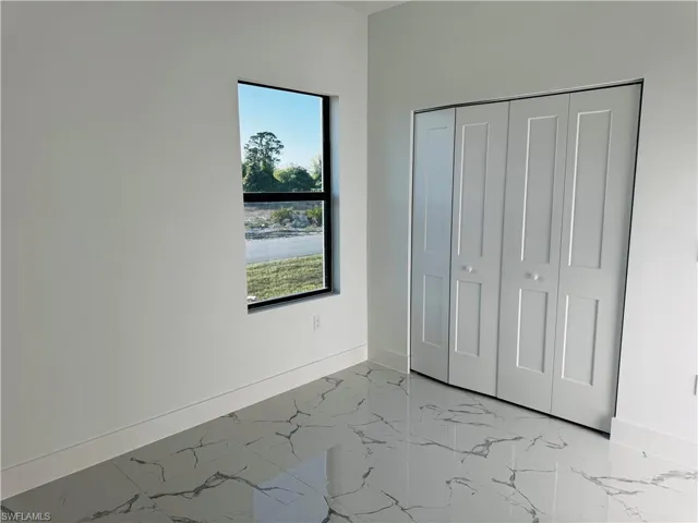 Unfurnished bedroom with marble finish floor, a closet, and baseboards