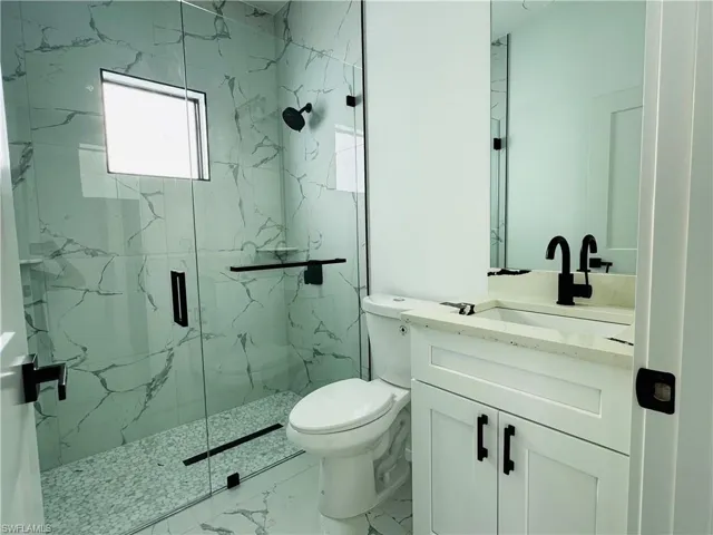 Bathroom with marble finish floor, toilet, vanity, and a marble finish shower
