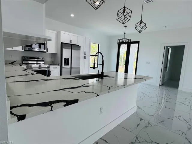 Kitchen featuring marble finish floor, appliances with stainless steel finishes, white cabinetry, a sink, and light stone counters