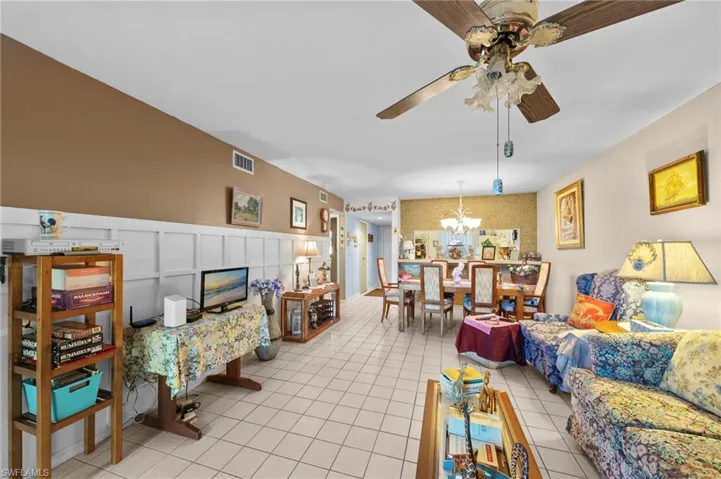 Living room featuring a decorative wall, ceiling fan, light tile patterned flooring, a wainscoted wall, and a chandelier