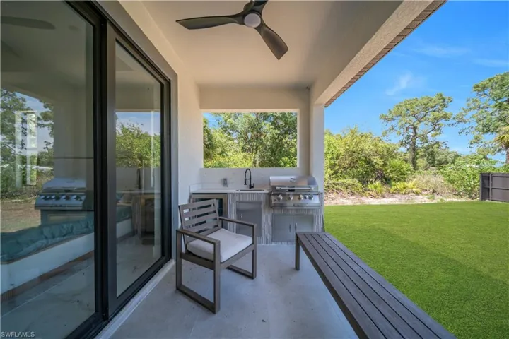 Covered outdoor patio featuring an integrated outdoor kitchen with a built-in grill and sink, a ceiling fan, and sliding glass doors