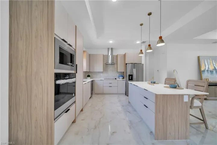 Contemporary kitchen featuring a spacious center island with seating, integrated stainless steel appliances, light wood-finish cabinetry, and marble-look tile flooring
