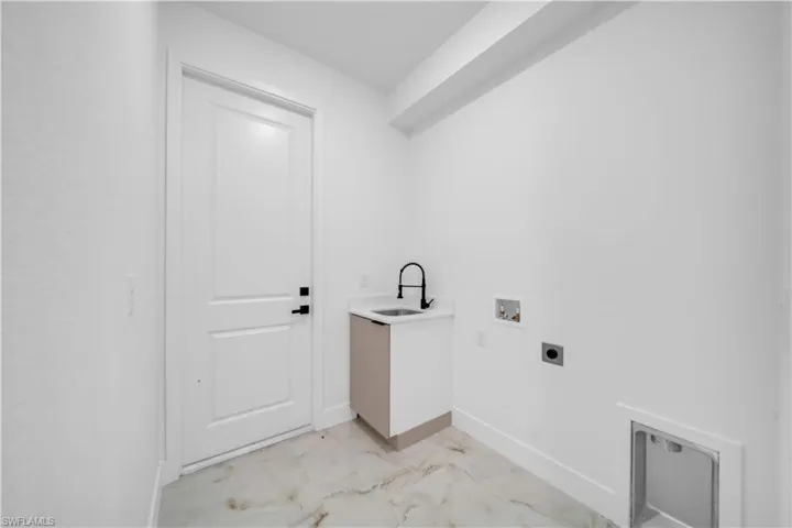 Utility room featuring a utility sink with a matte black faucet, washer/dryer hookups, and large-format tile flooring