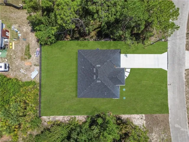 New construction residence featuring a dark shingle roof, a concrete driveway, and a manicured green lawn