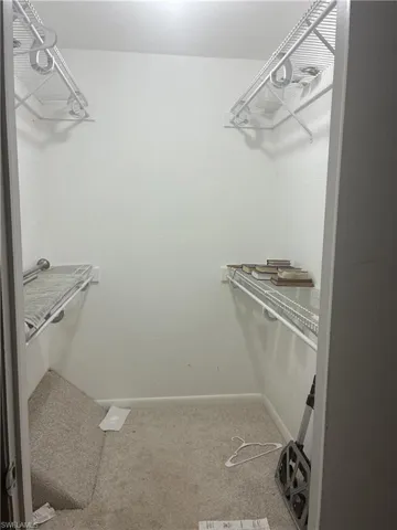 Walk-in closet featuring white wire shelving, hanging rods, and light-colored carpet flooring