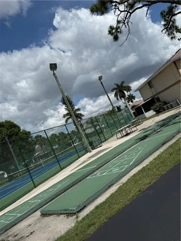 Shuffleboard courts alongside a tennis court, featuring a picnic table and overhead lighting
