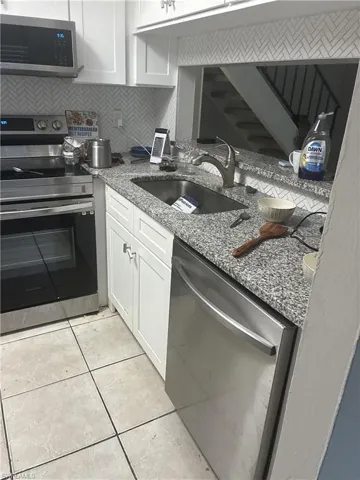 Kitchen featuring light-toned tile flooring, white shaker-style cabinetry, a stainless steel dishwasher, a stainless steel range with a built-in microwave, and speckled stone countertops