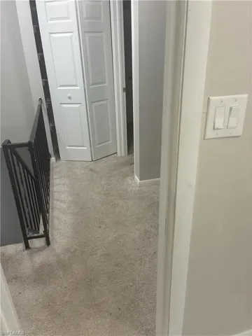 Carpeted hallway with light gray walls, a white bi-fold closet door, and a black metal stair railing