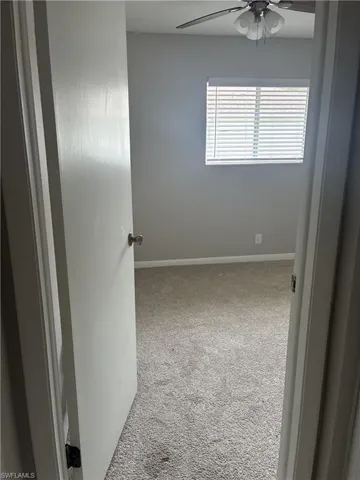 Carpeted interior room featuring neutral wall tones, a ceiling fan, and a window with horizontal blinds