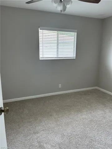 Carpeted room featuring a window with blinds, light gray walls, white baseboards, and a ceiling fan with light fixture
