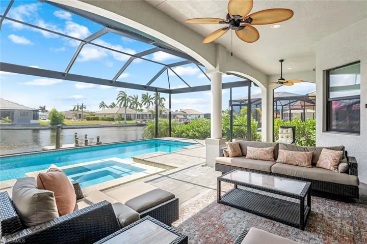 View of swimming pool with an outdoor living space, a water view, glass enclosure, a patio area, and ceiling fan