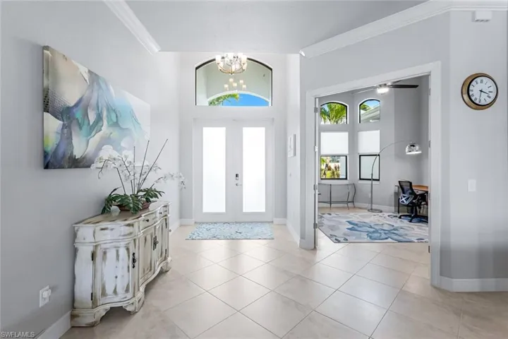 Foyer with light tile floors, french doors, crown molding, and ceiling fan with notable chandelier