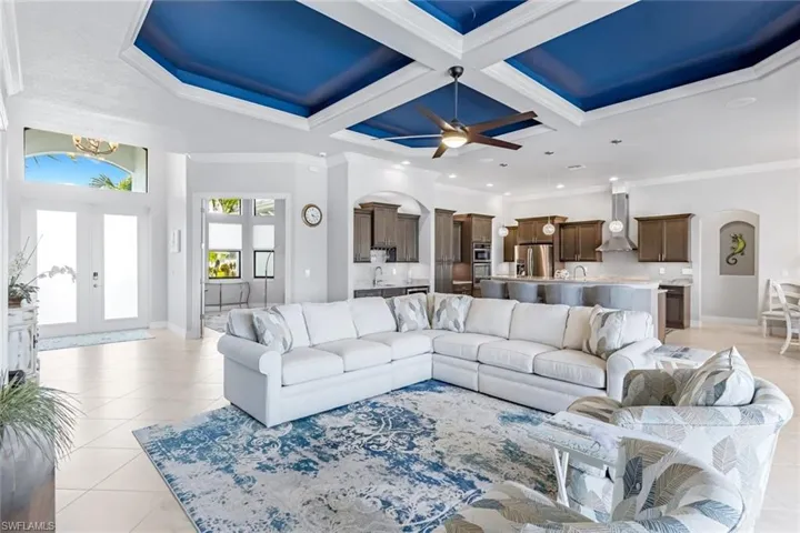 Living room with coffered ceiling, ceiling fan, ornamental molding, french doors, and light tile floors