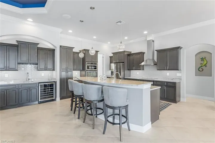 Kitchen with wall chimney range hood, stainless steel appliances, decorative light fixtures, wine cooler, and tasteful backsplash