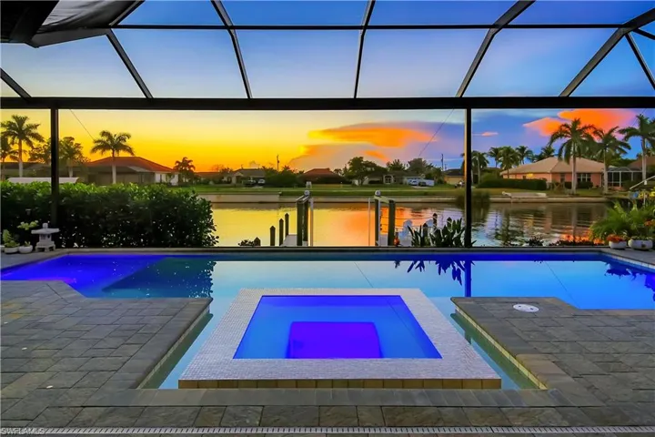 Pool at dusk featuring a lanai, an in ground hot tub, and a water view