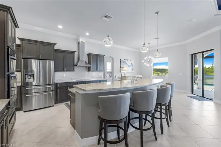 Kitchen featuring decorative light fixtures, stainless steel appliances, backsplash, a kitchen island with sink, and wall chimney exhaust hood