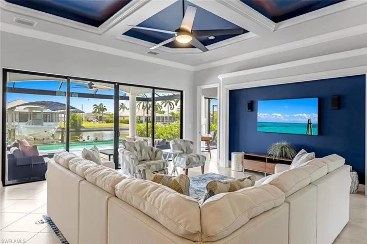 Tiled living room featuring a water view, ornamental molding, ceiling fan, and coffered ceiling