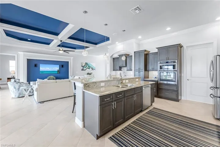Kitchen featuring coffered ceiling, stainless steel appliances, ceiling fan, an island with sink, and sink