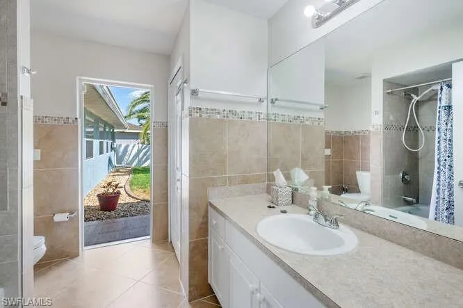 Bathroom with tile patterned flooring, vanity, tile walls, and toilet