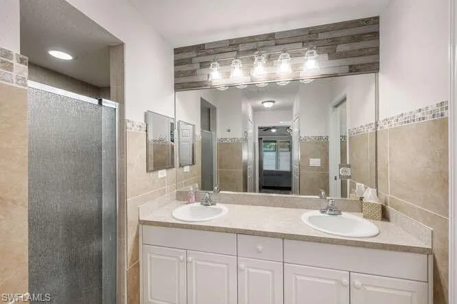 Bathroom with vanity, a shower with shower door, and tile walls