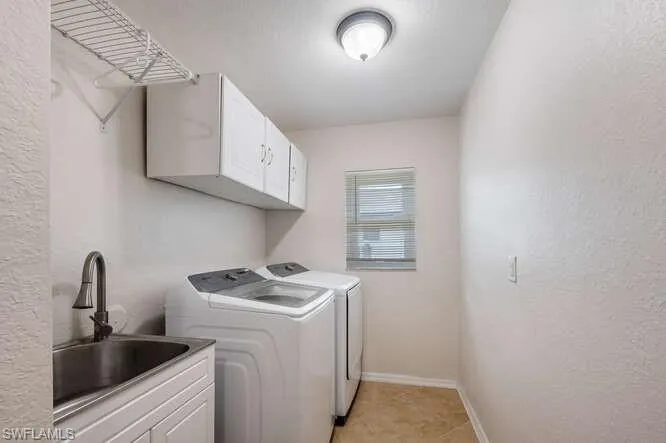 Laundry area featuring cabinets, sink, light tile patterned floors, and washing machine and clothes dryer