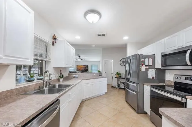 Kitchen featuring sink, light tile patterned floors, ceiling fan, appliances with stainless steel finishes, and white cabinetry