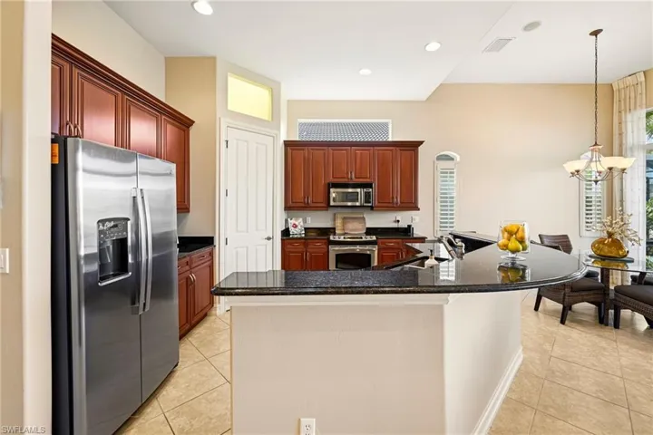 Kitchen with stainless steel appliances, a large island, light tile patterned flooring, and dark stone counters