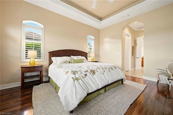 Bedroom with a closet, dark wood finished floors, ornamental molding, a ceiling fan, and a raised ceiling
