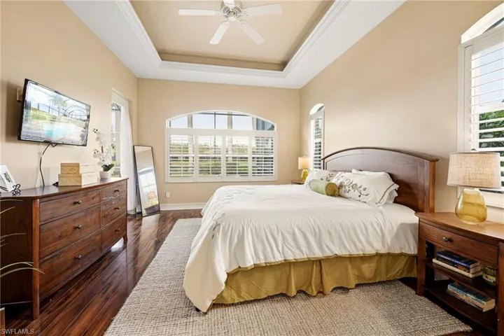 Bedroom featuring dark wood-type flooring, ceiling fan, ornamental molding, and a tray ceiling