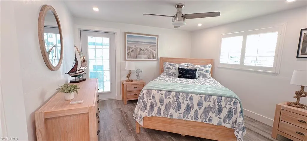Recessed lighting illuminates wood-finish flooring in this room featuring a ceiling fan, a full-lite exterior door, and plantation shutters