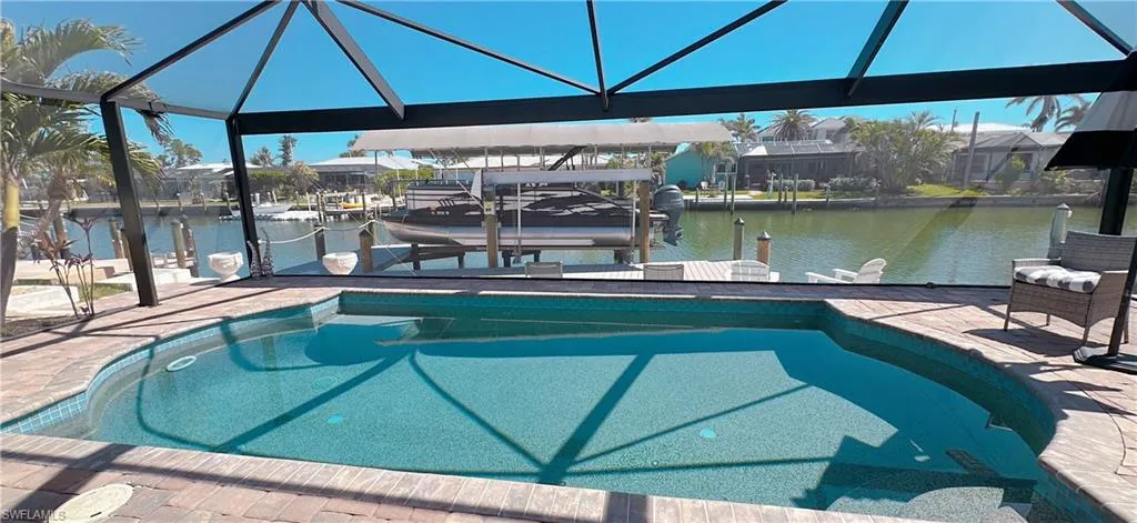 Screened-in pool deck featuring a geometric pool with mosaic tile trim, brick paver coping, and direct waterfront access with a private boat dock and lift