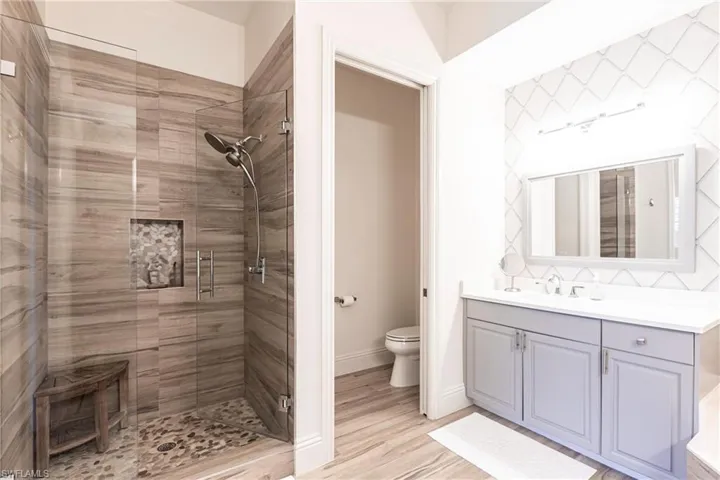 Bathroom featuring vanity, toilet, a stall shower, baseboards, and wood finished floors