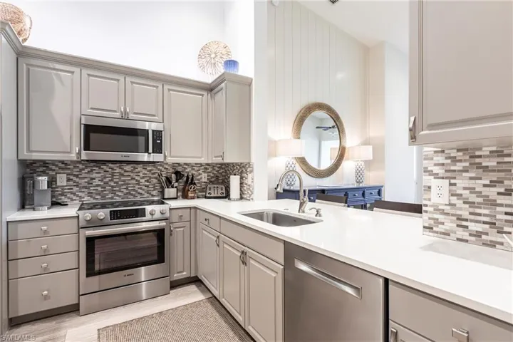 Kitchen with gray cabinets, appliances with stainless steel finishes, light countertops, and a sink