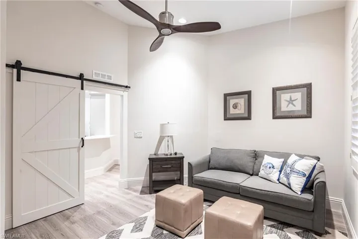 Living area with wood finished floors, a barn door, ceiling fan, baseboards, and visible vents