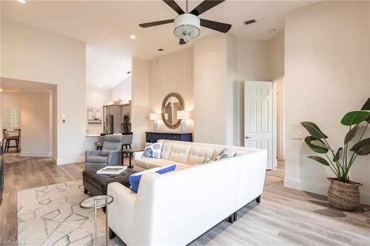 Living area with ceiling fan, visible vents, baseboards, light wood-type flooring, and high vaulted ceiling