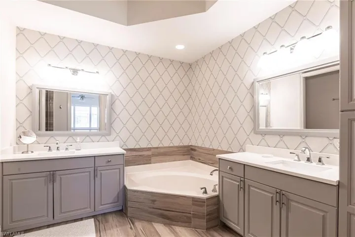 Bathroom with a garden tub, two vanities, a sink, and wood finished floors