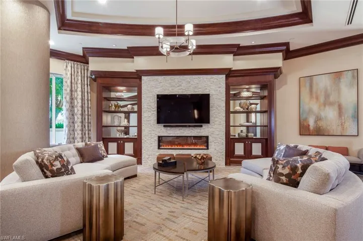 Living area featuring a glass covered fireplace, built in features, ornamental molding, and a tray ceiling