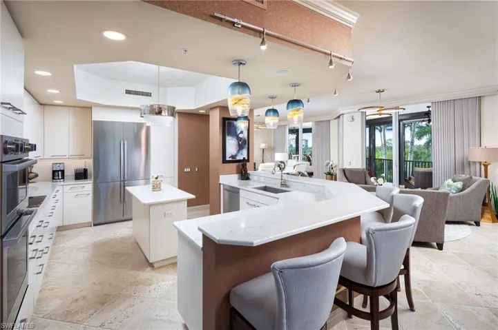 Kitchen featuring hanging light fixtures, stainless steel appliances, white cabinetry, track lighting, and light stone countertops