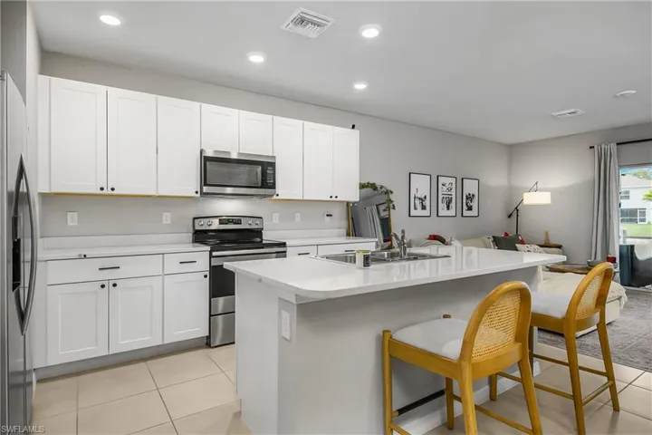 Kitchen featuring appliances with stainless steel finishes, an island with sink, open floor plan, white cabinetry, and light tile patterned flooring