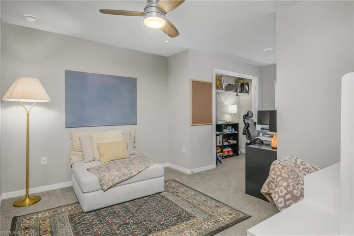 Bedroom with ceiling fan, an office area, and light colored carpet