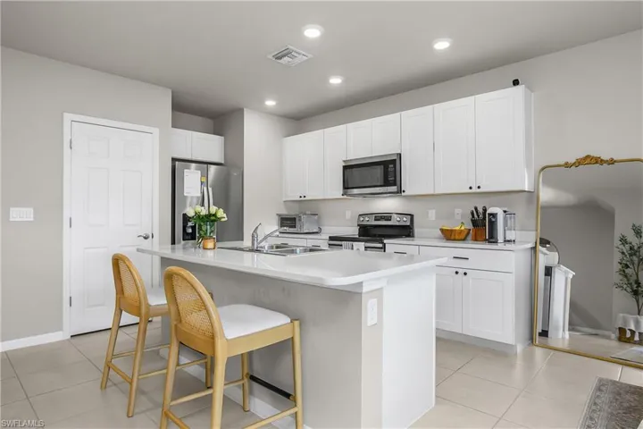 Kitchen featuring light countertops, stainless steel appliances, white cabinets, a kitchen breakfast bar, and an island with sink