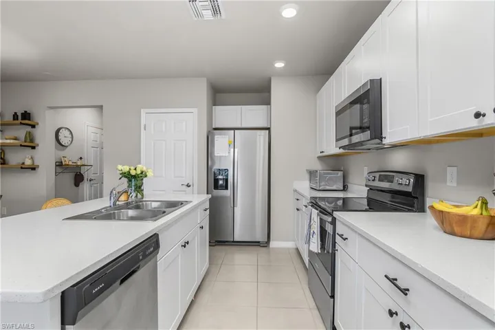 Kitchen featuring stainless steel appliances, white cabinets, an island with sink, light tile patterned floors, and recessed lighting